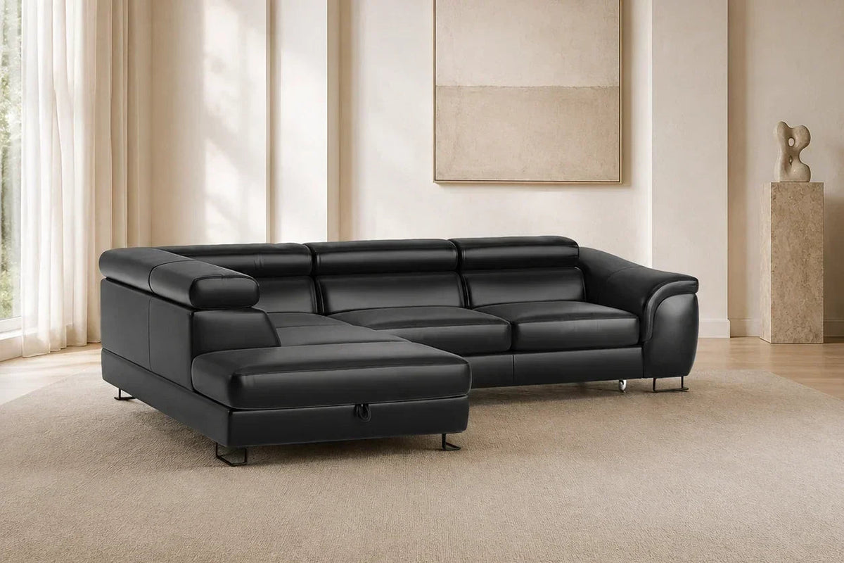 A modern black leather sectional sofa with a chaise lounge, positioned on a large beige area rug in a minimalist, warm-toned living room.